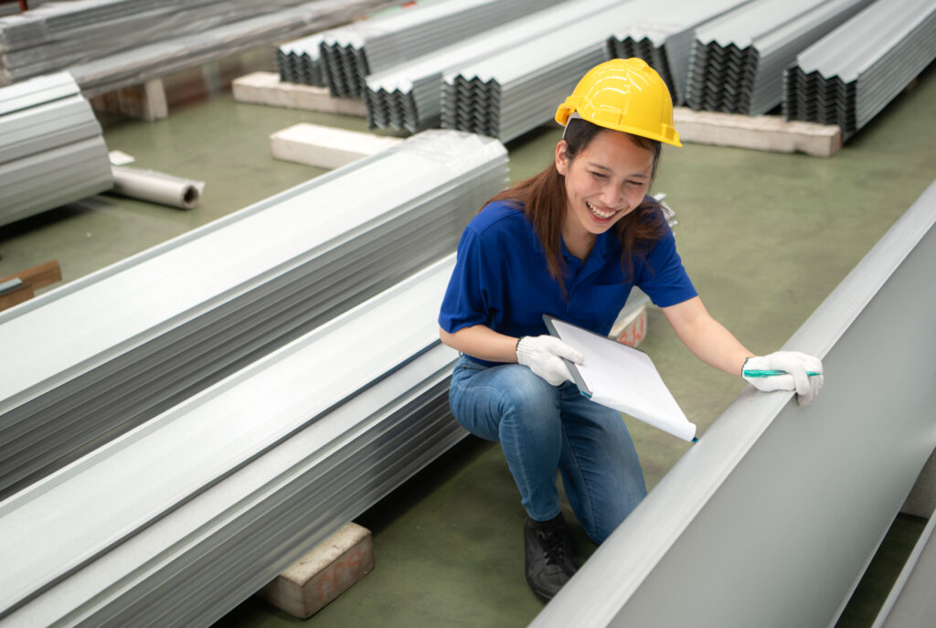 Jeune ouvrière discute et inspecte des plaques d'acier destinées au formage polyvalent avant l'envoi sur la chaîne de production d'une usine.